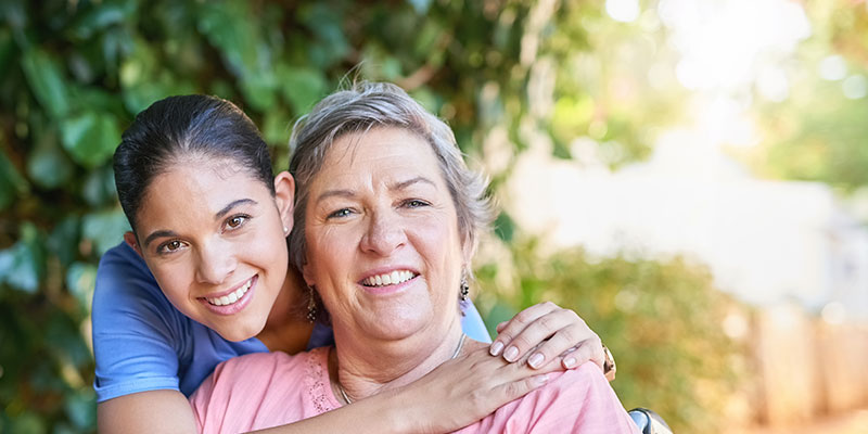 Two smiling women embrace in a green outdoor setting.