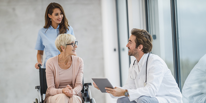 Successful doctor and young nurse talking with their senior female wheelchair-bound patient.
