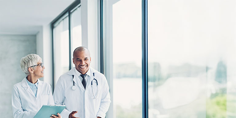 Two doctors smiling and walking through a hallway.