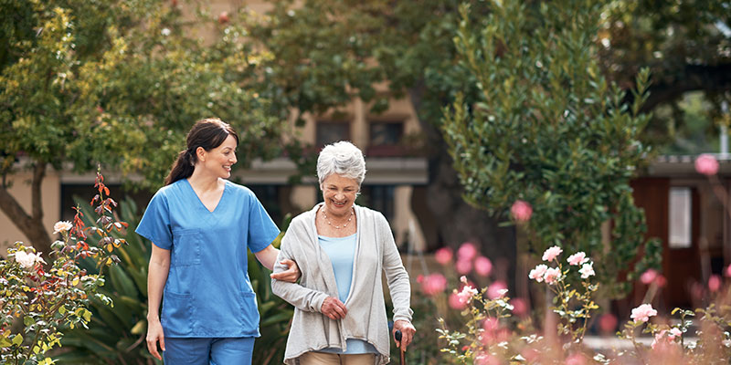 Nurse assisting elderly woman in a garden.
