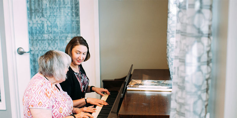 Two women playing piano together in a bright room.