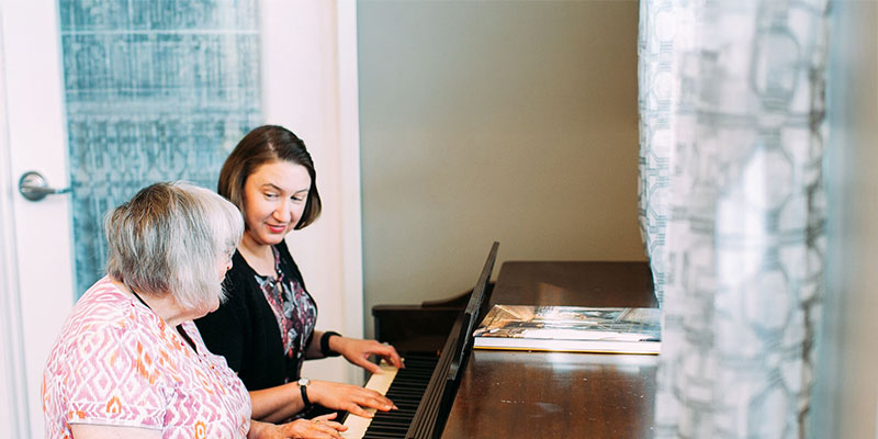 Two women playing piano together in a cozy setting.